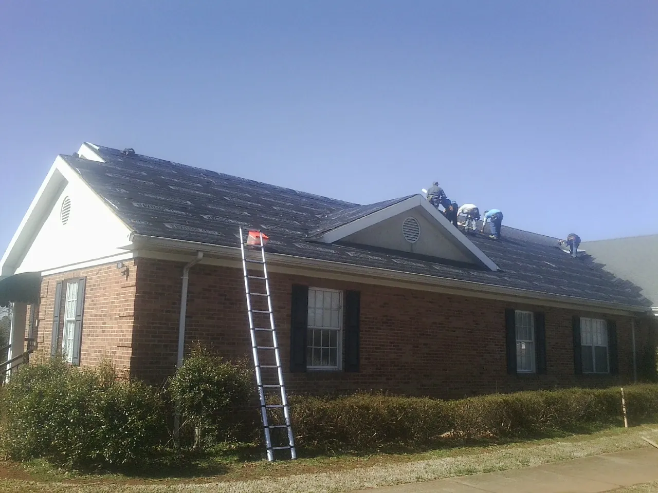 Crew tearing shingles off a brick ranch roof with a ladder set — Emergency Roof Repair work by our crew in Graham