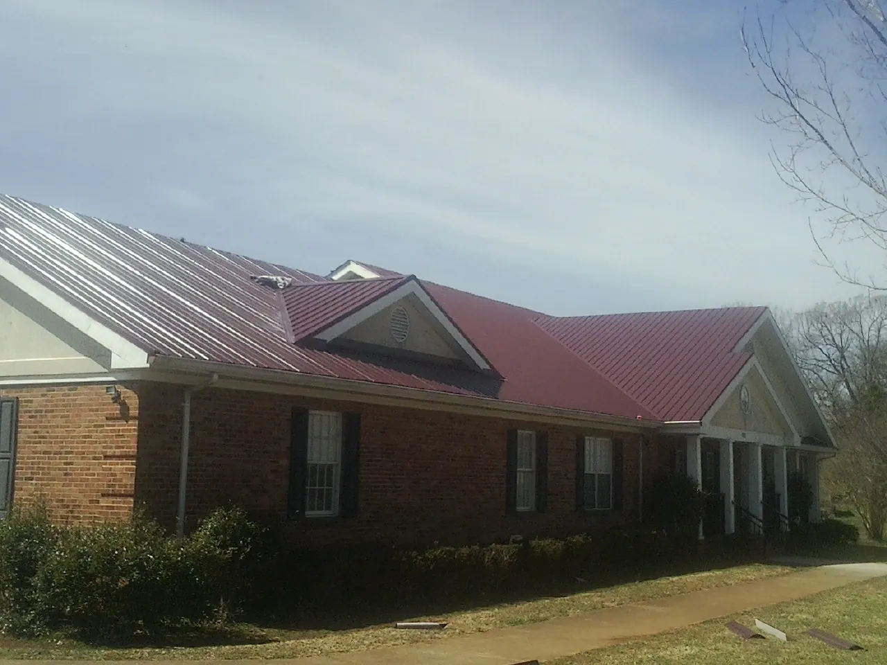 Red metal roof with gabled entries on a long brick building, from a Hail Damage Roof Repair job in Graham