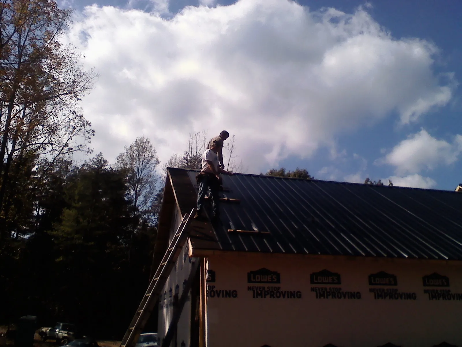 Roofer fastening dark metal panels high against a cloudy sky, from a Roof Inspection job in Graham