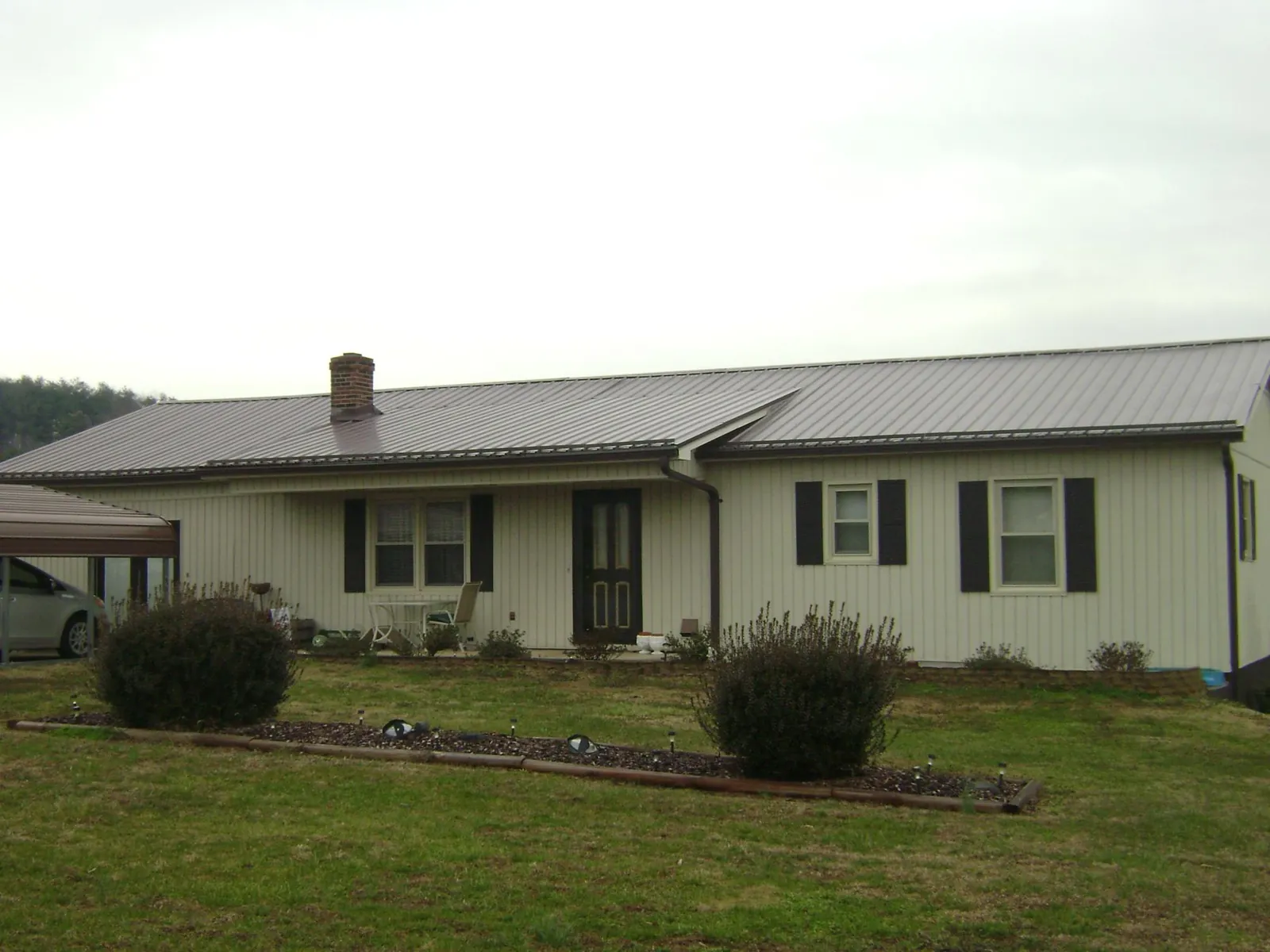 Brown metal roof on a cream sided ranch home with a brick chimney in Graham