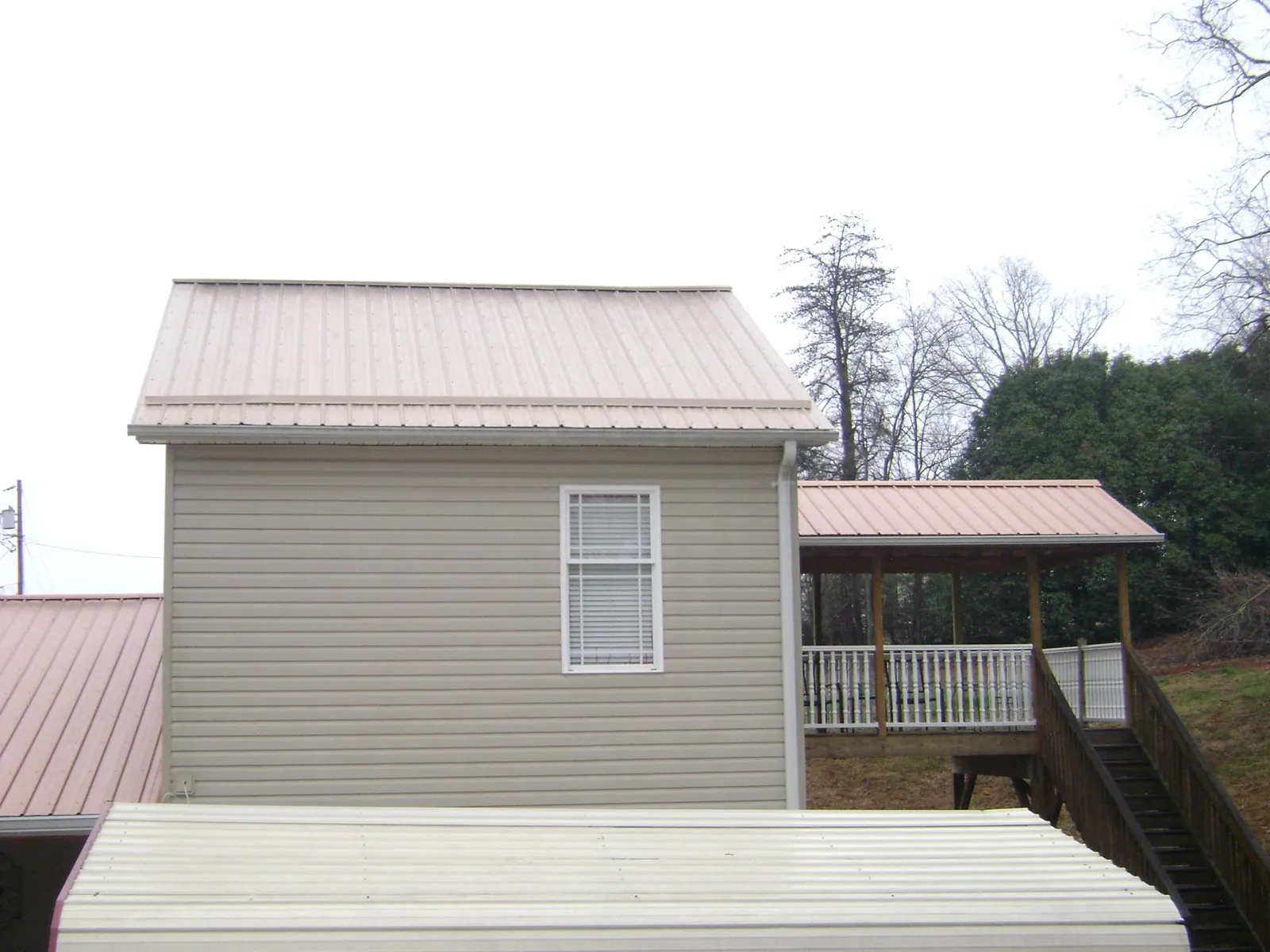 Tan metal roofs on a two story addition and attached porch, from a Roof Replacement job in Graham
